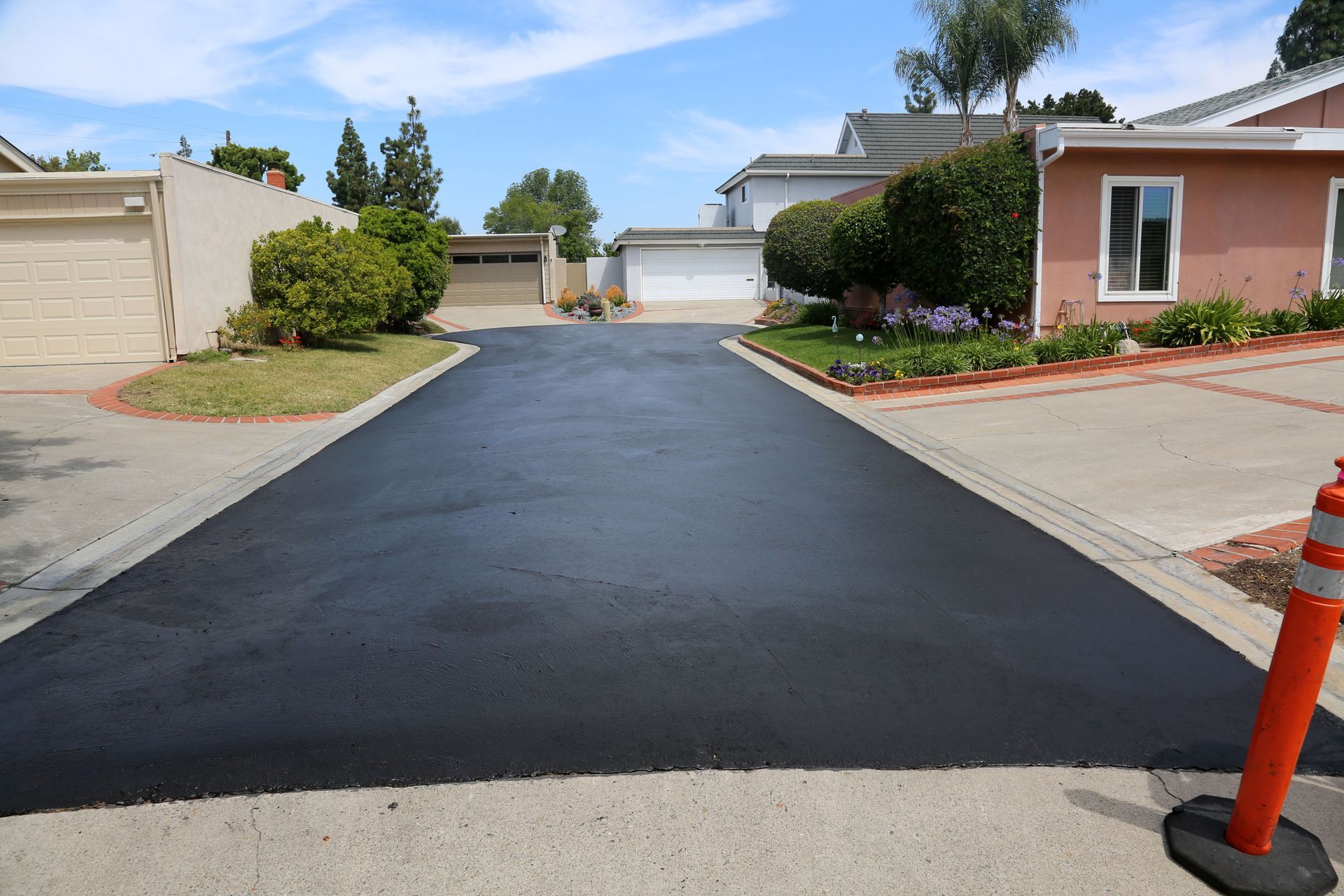 Black asphalt driveway in front of houses; orange traffic cone on the right.