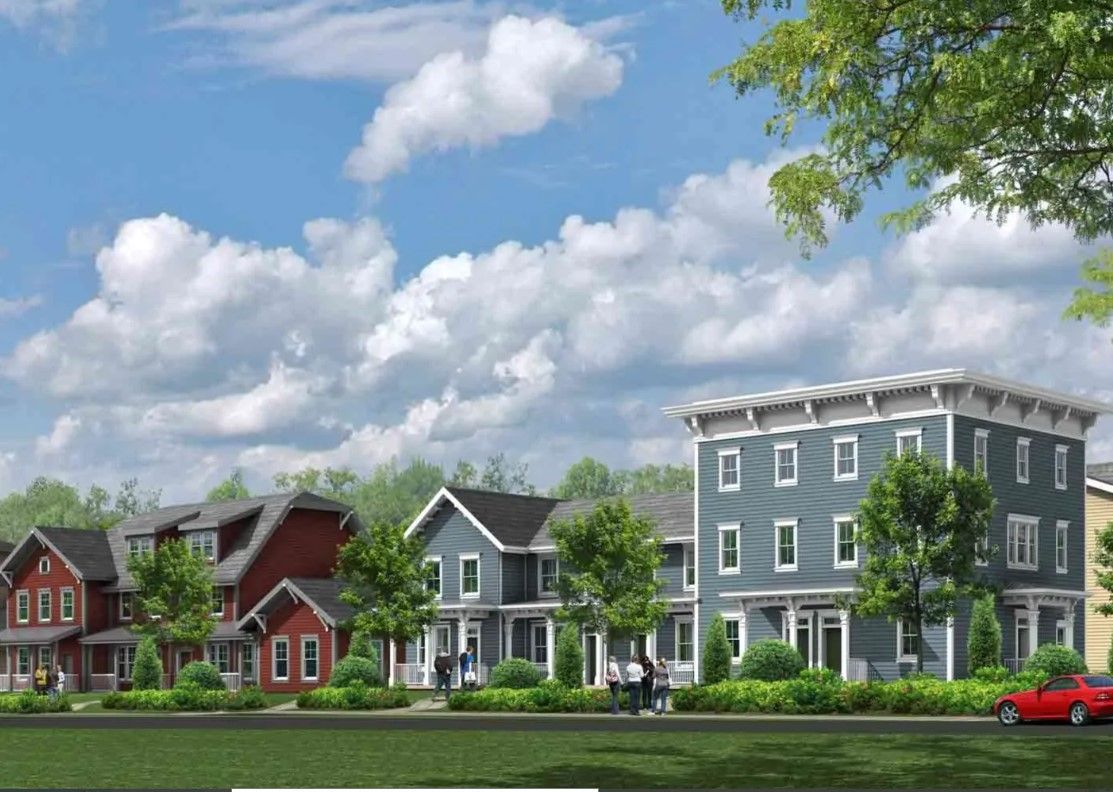Row of colorful townhouses under a blue sky; trees and a red car in the foreground.