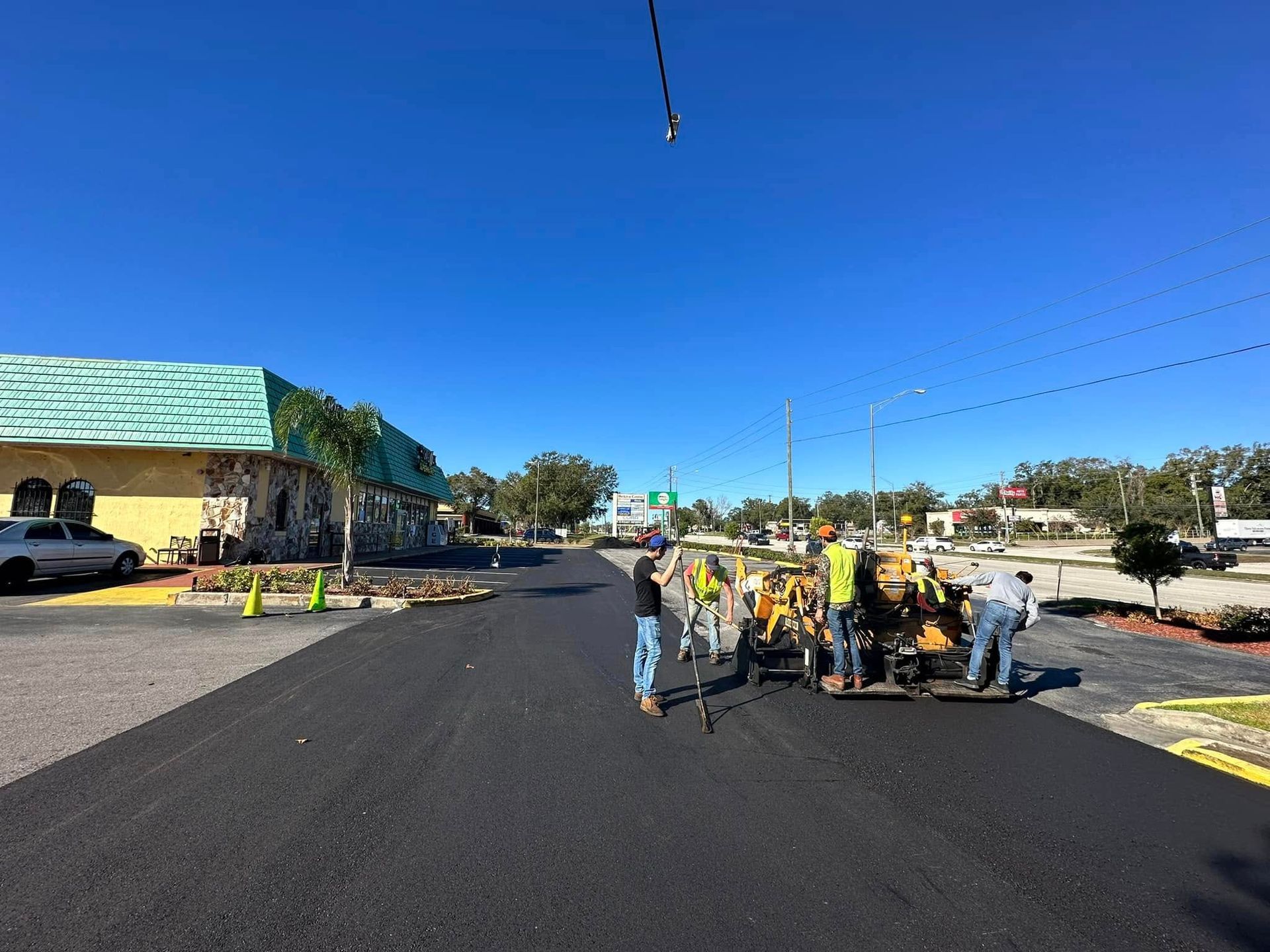 Roadwork crew in safety vests paving a street under a bright blue sky