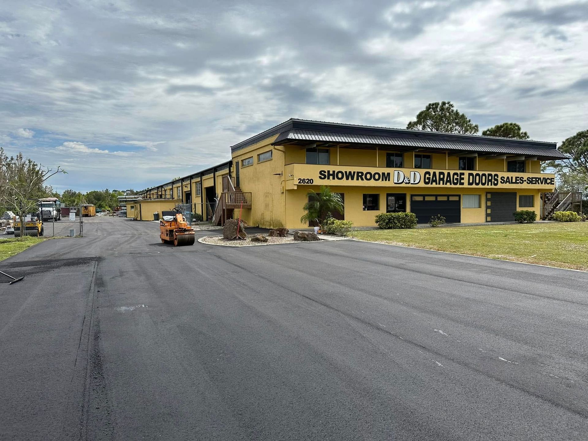Yellow garage building with black awning beside a newly paved road under cloudy skies