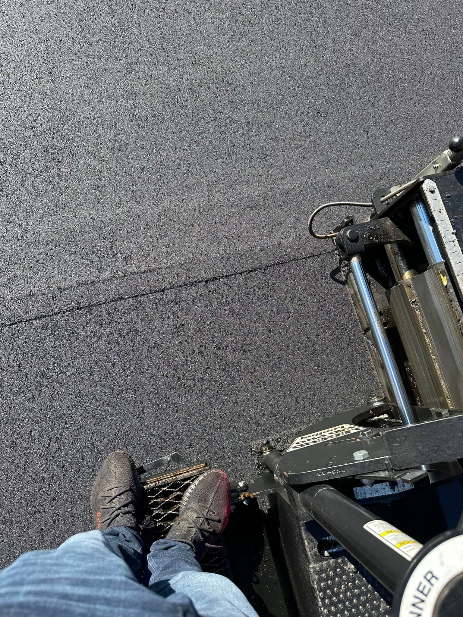 Person standing on a metal platform above gray asphalt, wearing black shoes and blue jeans.