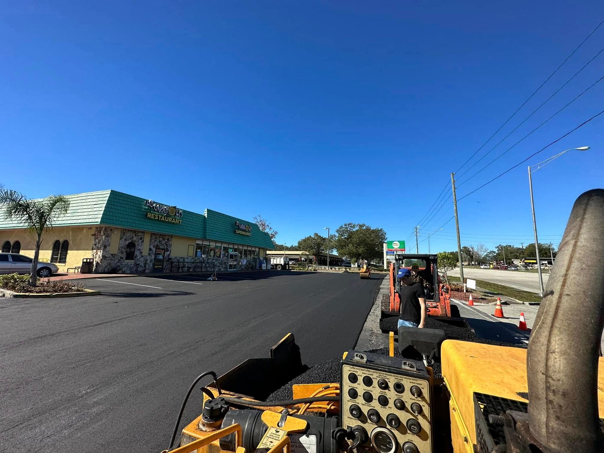 Roadside construction view with yellow machinery, a wide street, and a blue sky.
