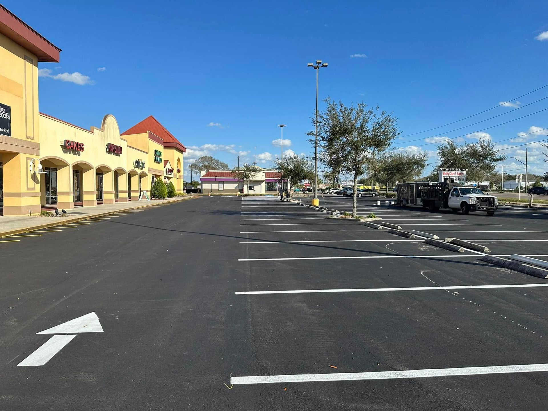 Empty shopping center parking lot with marked spaces and storefronts on a sunny day