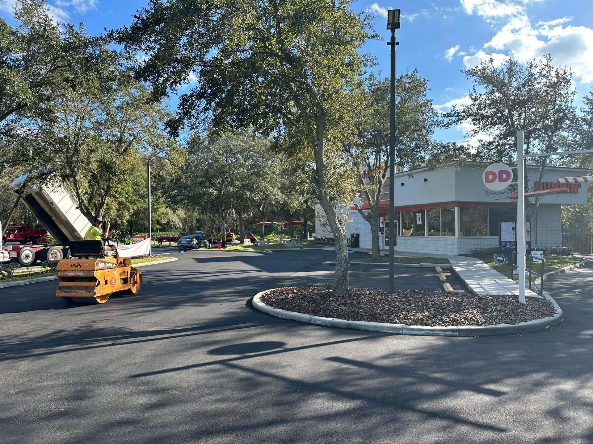 Parking lot with a portable sign and a Doughnut store, surrounded by trees under a blue sky.