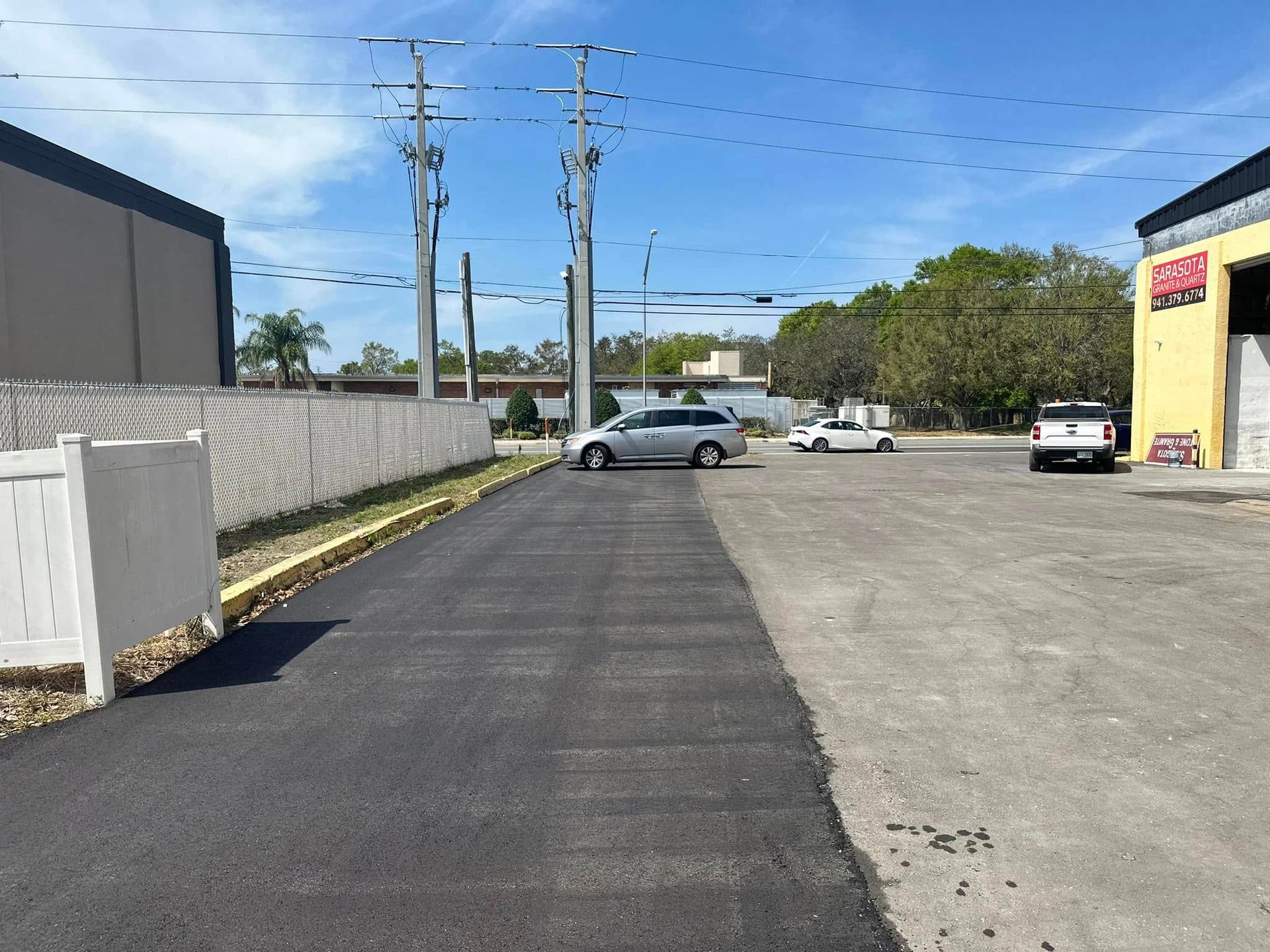 Outdoor parking lot with a parked silver car beside a yellow building and concrete wall.