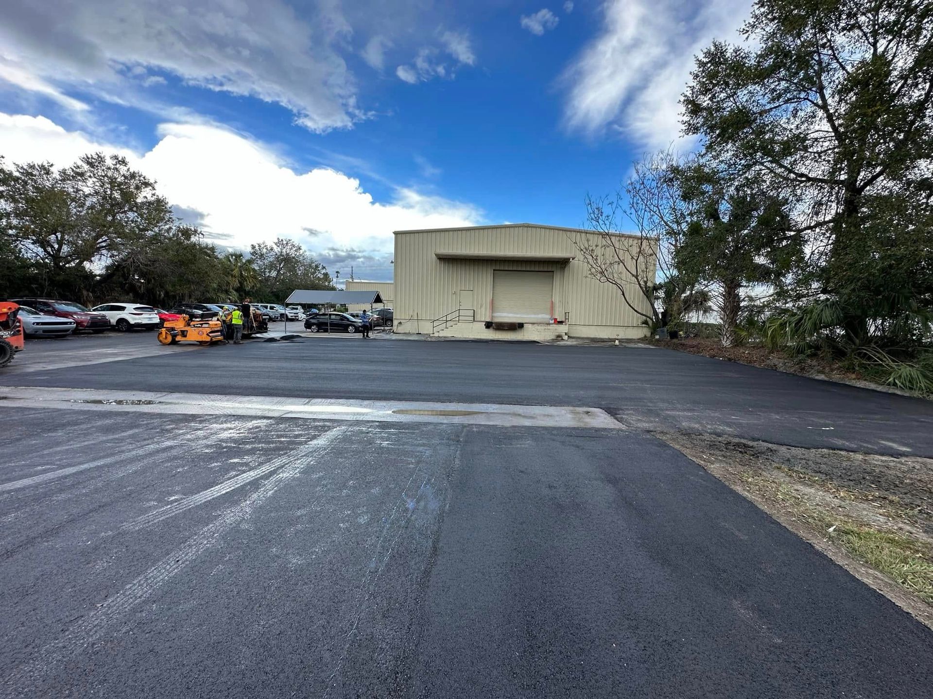 Empty asphalt lot with a beige tent building under a partly cloudy blue sky