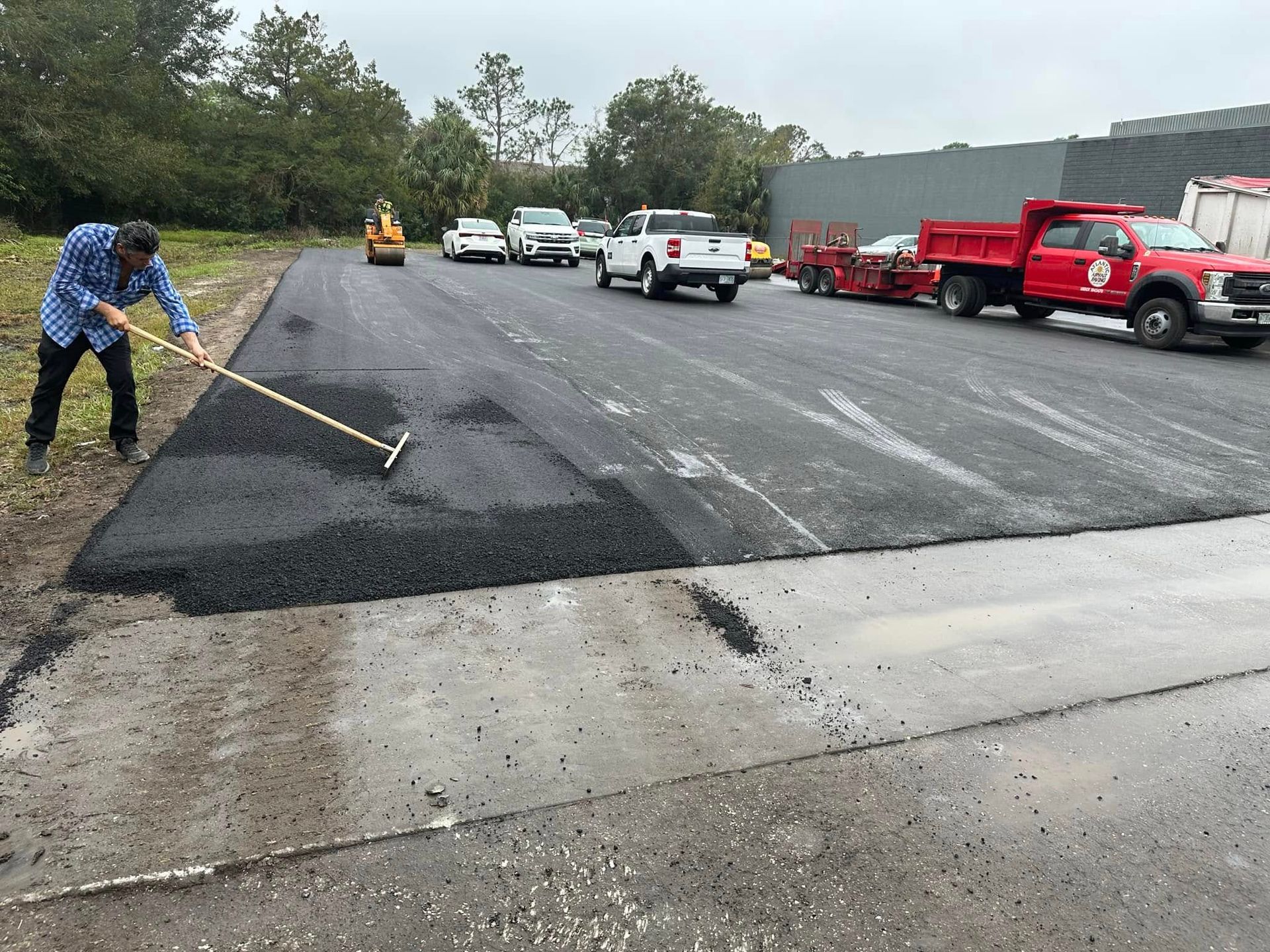 Road crew patching wet highway pavement with trucks and equipment nearby