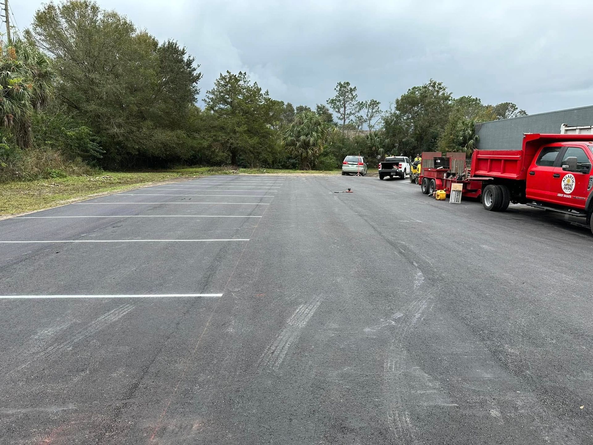 Wide gravel parking lot beside trees, with several vehicles and red utility trucks parked along the right side.