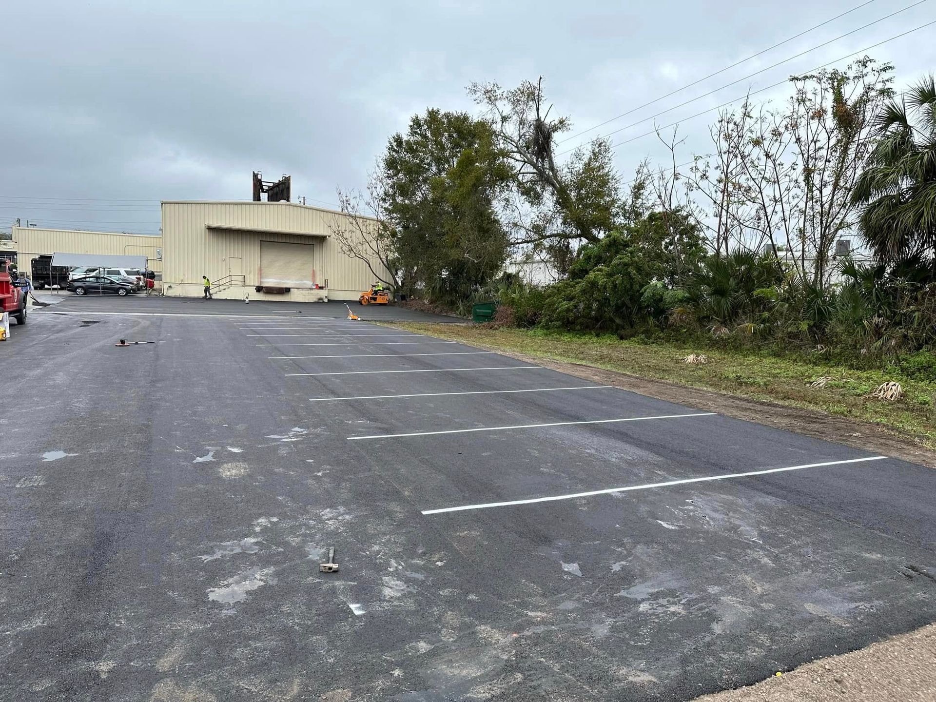 Empty parking lot beside a beige building and trees under a cloudy sky