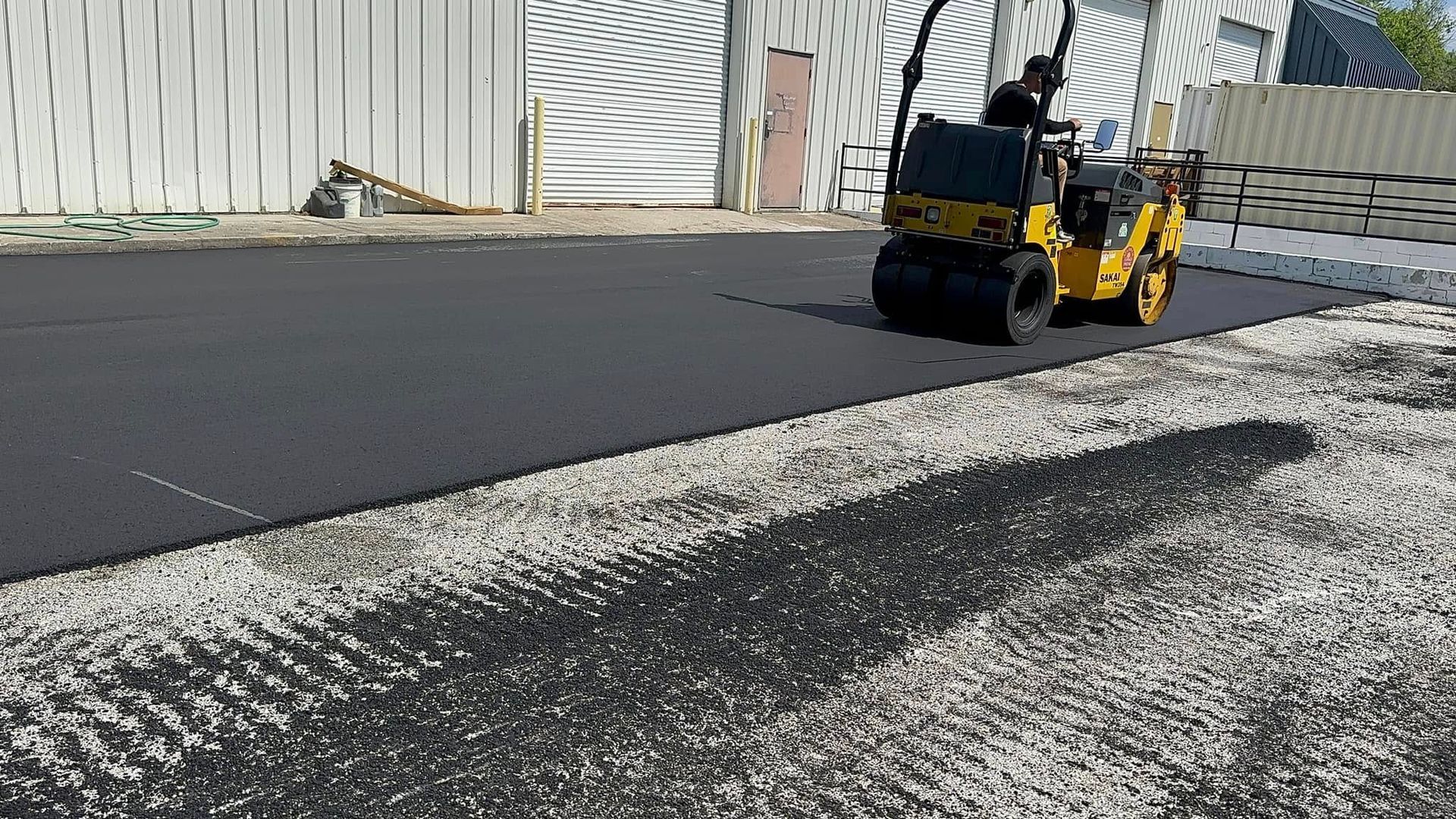Yellow road roller compacting asphalt on a road beside a white building