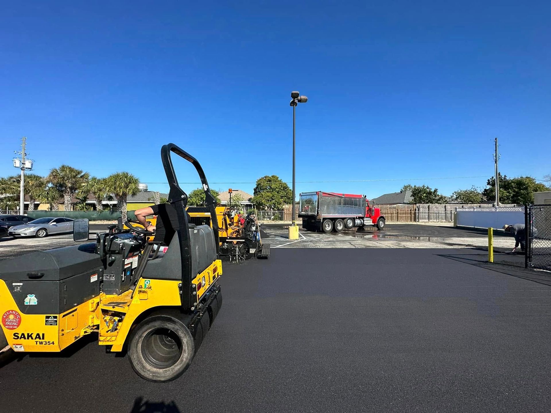 Yellow utility vehicle and workers in a parking lot under a clear blue sky