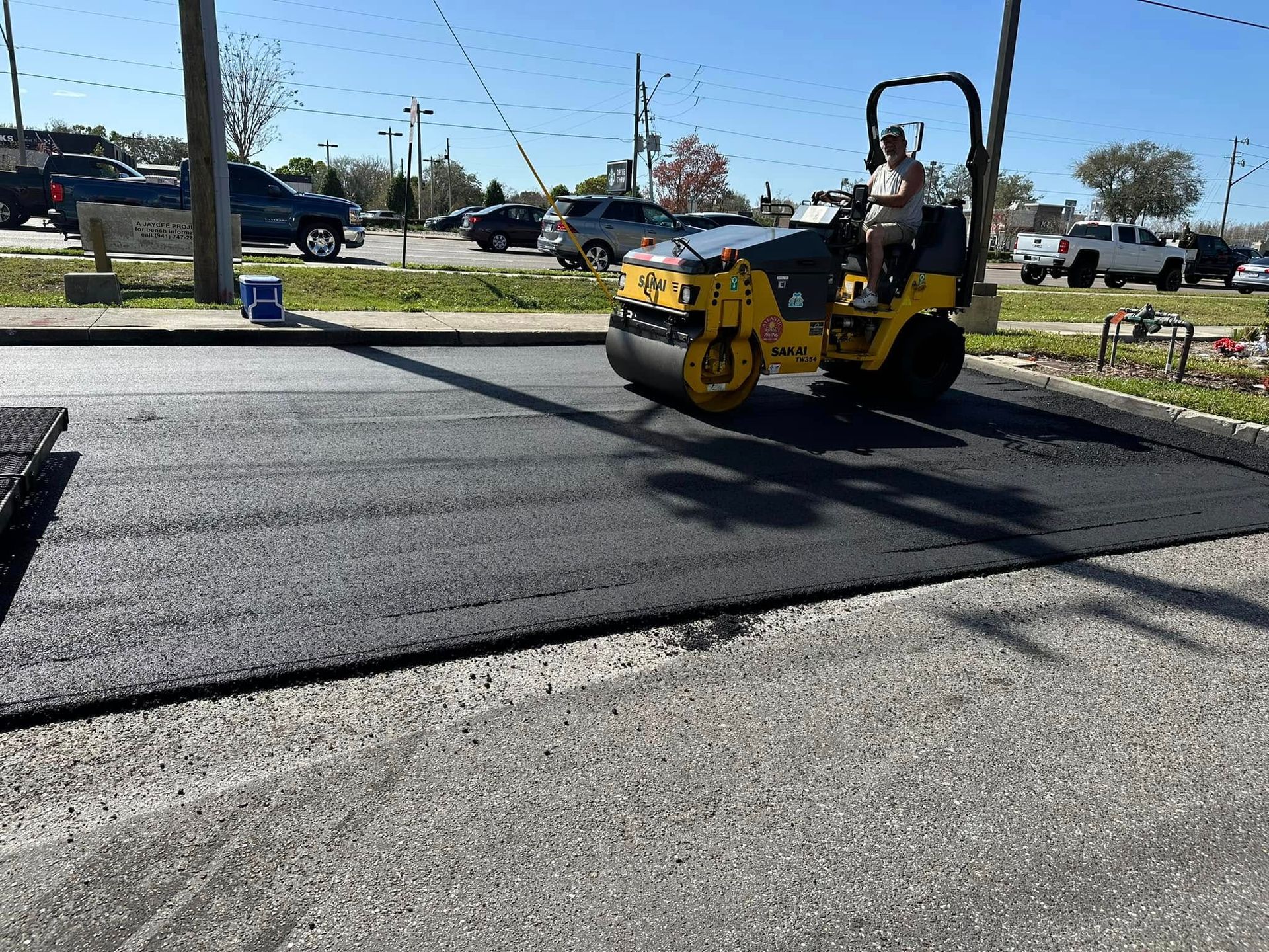 Yellow road roller paving a black asphalt road on a sunny day