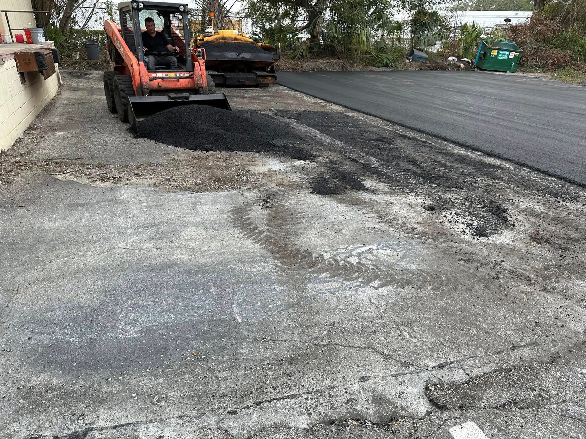 Orange skid steer grading gravel beside a paved road at a construction site