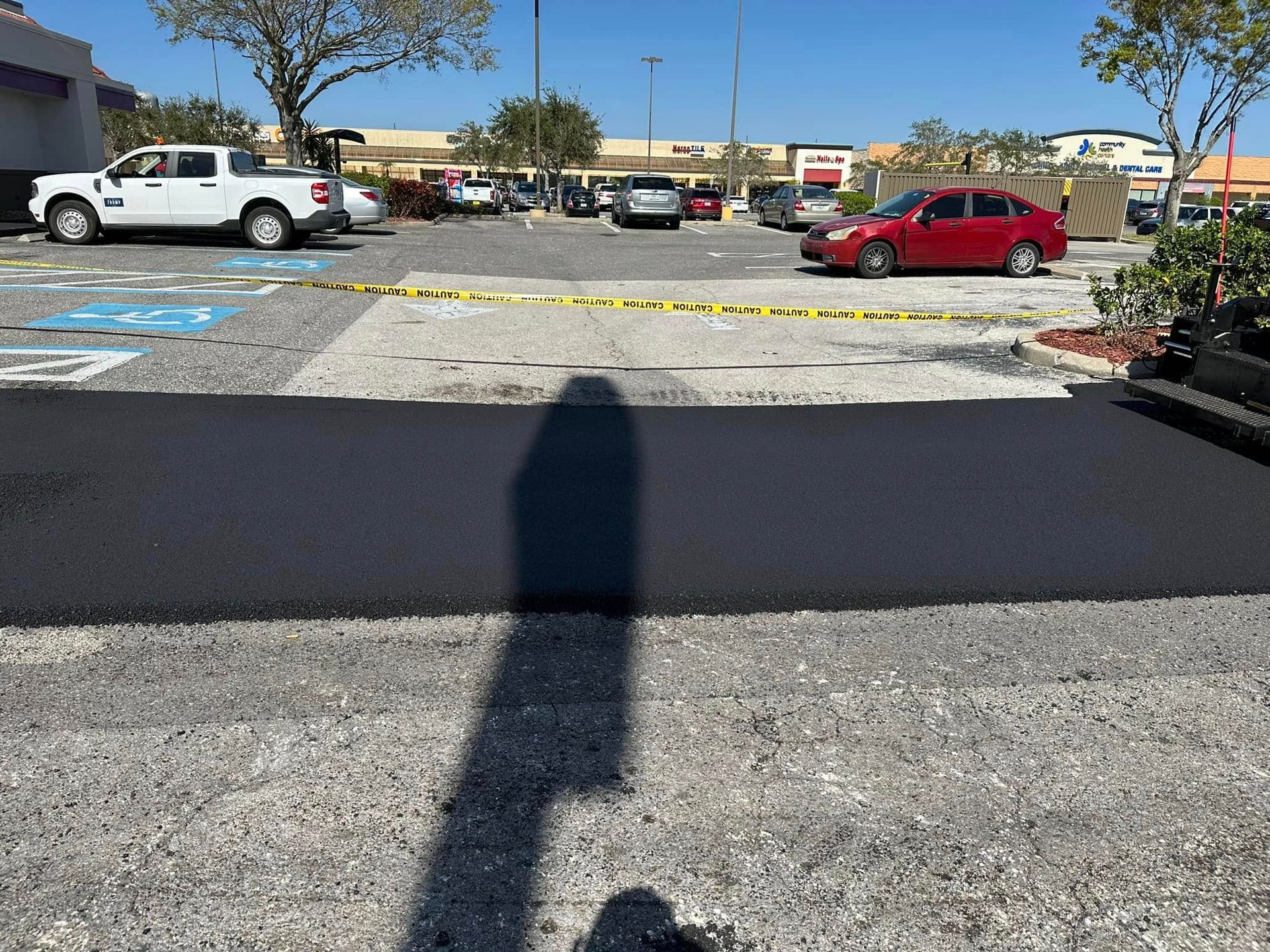 Parking lot with parked cars, a building in the background, and a dark shadow across the pavement.