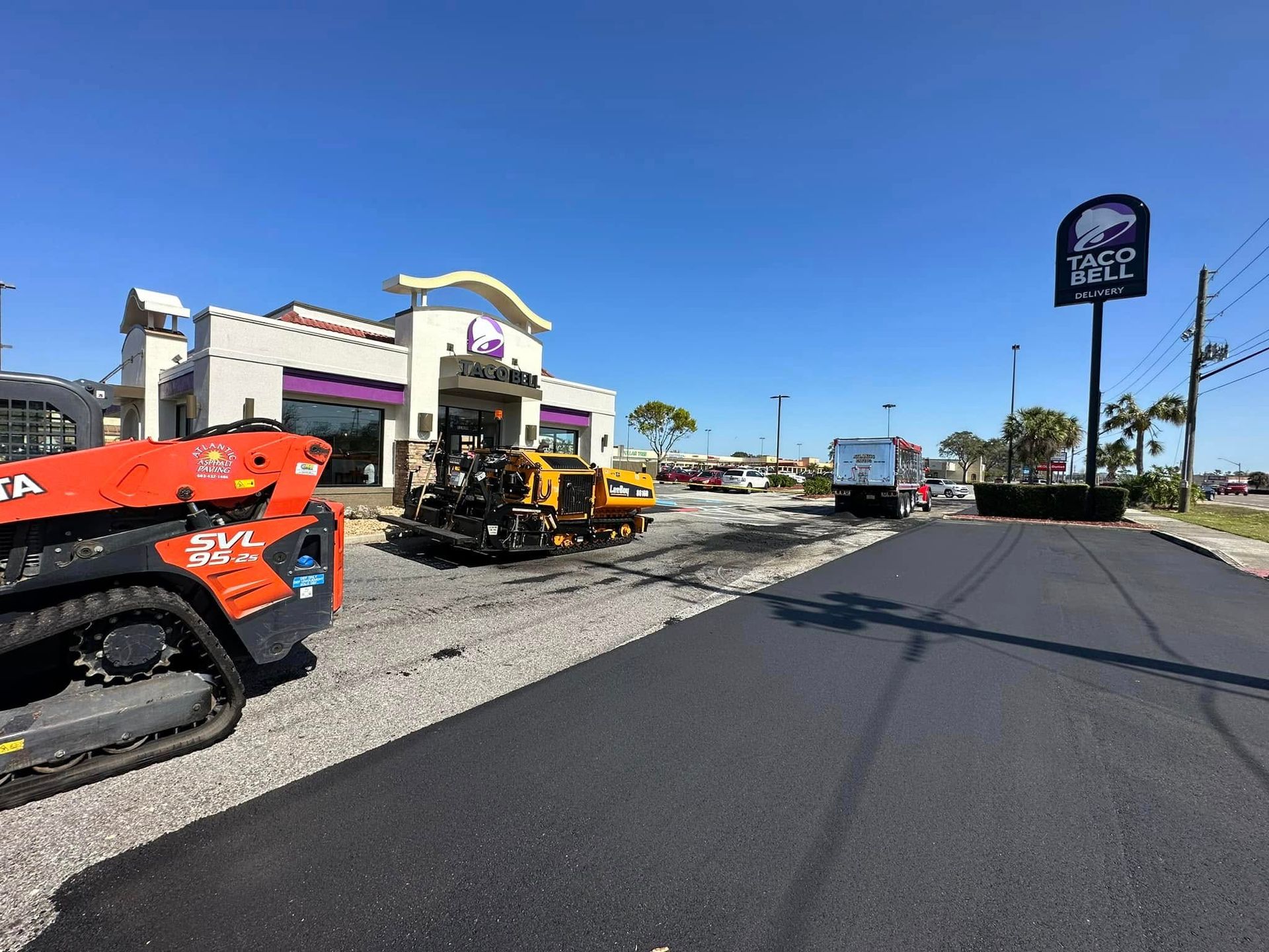 Roadside construction near a mall entrance with orange equipment and a tall sign on a sunny day