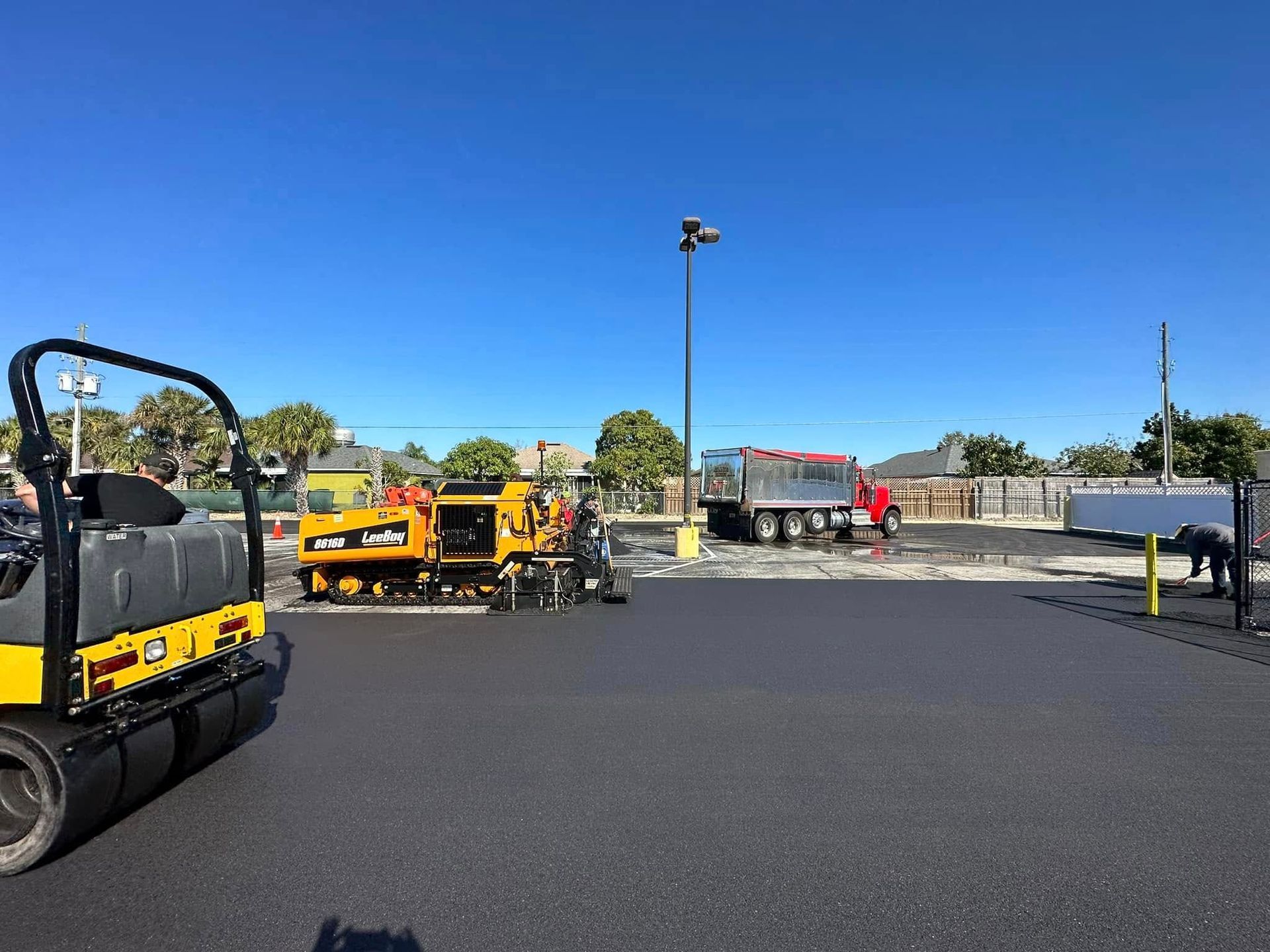 Paved lot with construction equipment, including a yellow roller, under a clear blue sky