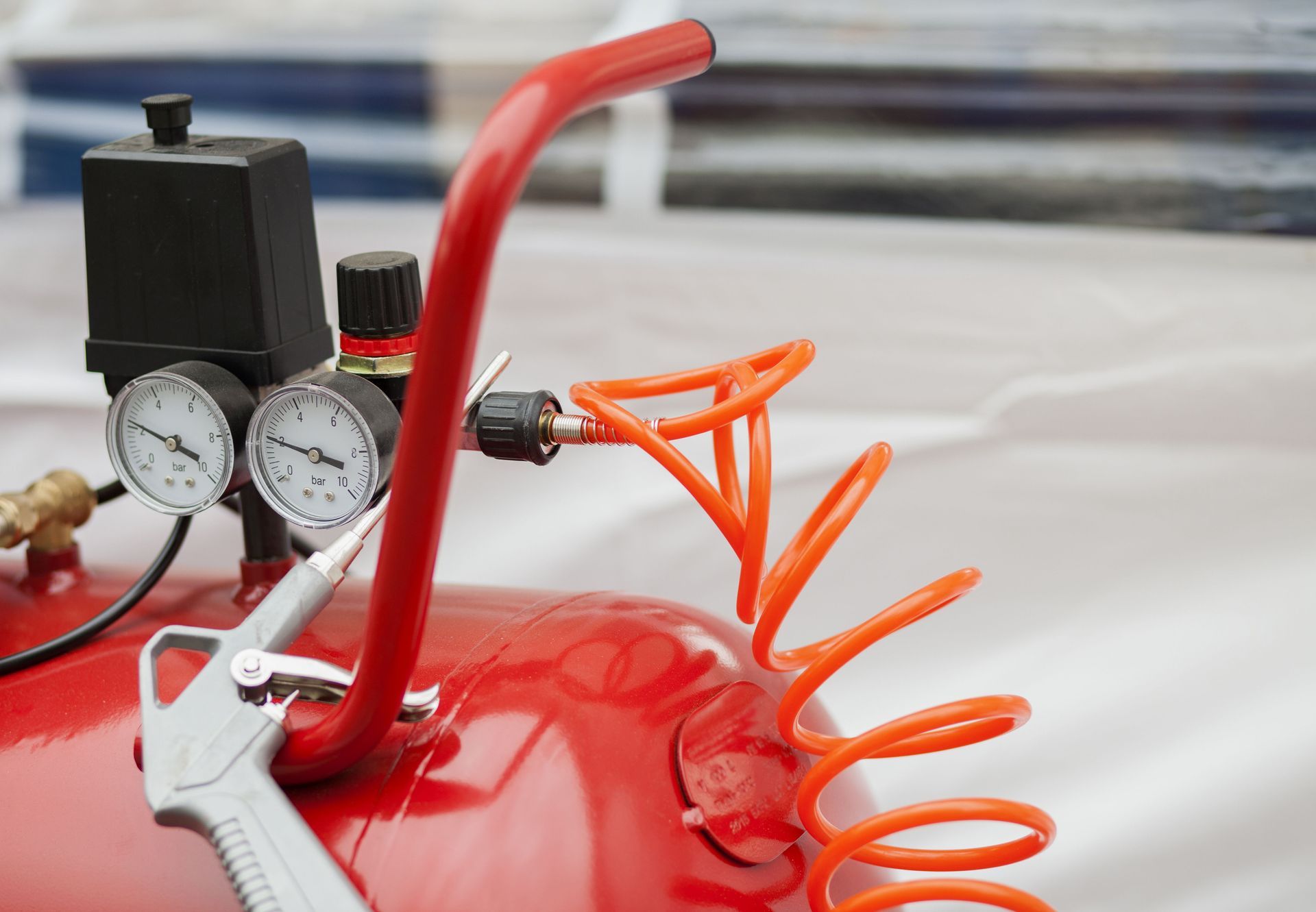 A red air compressor with two pressure gauges, a black power switch, and an attached orange coiled air hose.
