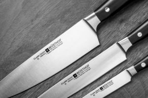 Three Wüsthof Classic Ikon knives of varying sizes arranged diagonally on a dark wooden surface.