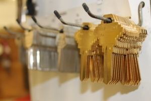 Rows of gold-colored blank keys hanging on metal hooks against a white wall.