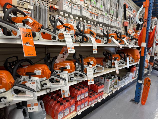 Shelves in a retail store stocked with orange and white Stihl chainsaws and bottles of engine oil.