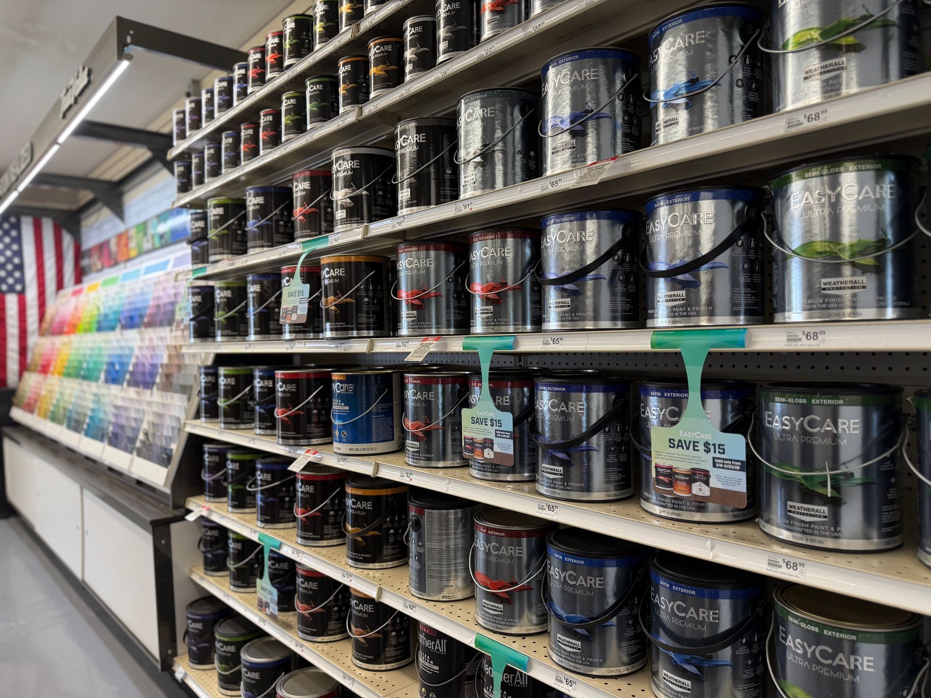 Shelves stocked with various sizes and brands of paint cans in a retail store, with a color swatch display on the left.