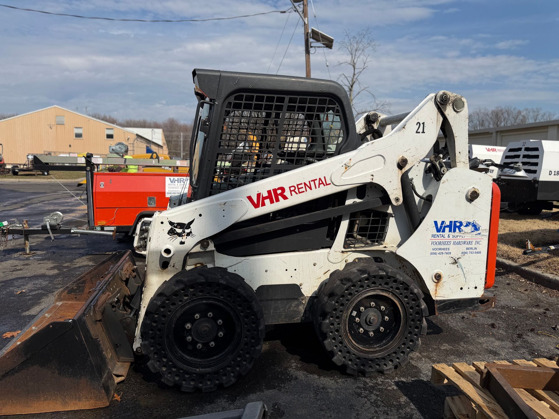 A white Bobcat skid-steer loader with VHR Rental branding parked outdoors on an asphalt lot.