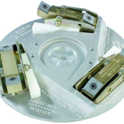 A circular mechanical metal part features three symmetrically mounted brass-colored clamping blocks with directional arrows.