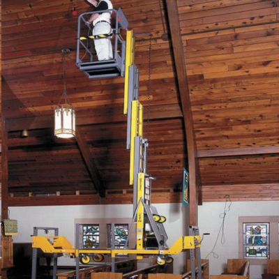 A person standing on a yellow, telescoping vertical mast lift works on the ceiling of a wood-paneled room.