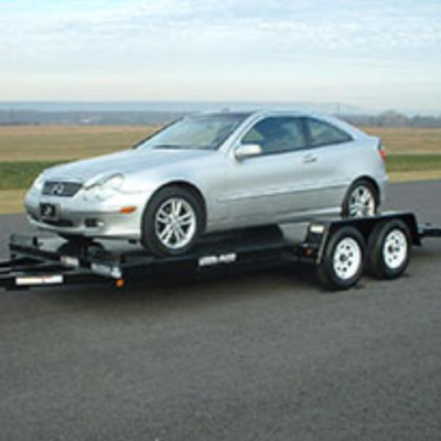 A silver coupe car is securely loaded onto a flatbed car hauler trailer parked on an asphalt lot.