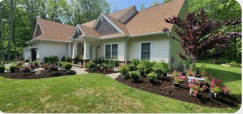 A white house with a brown roof and landscaping in front, with a green lawn.