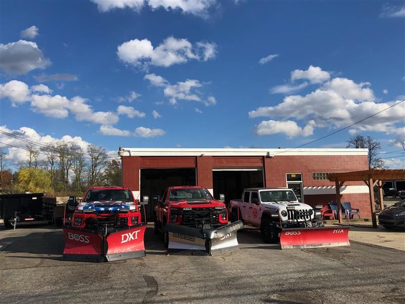 Three trucks with snow plows parked in front of a red building under a partly cloudy sky.