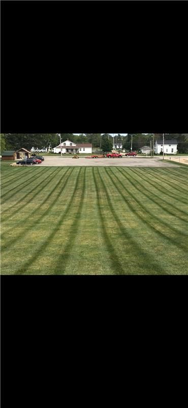 Lawn cut in neat stripes in front of buildings. A vehicle is on the edge of the grass.