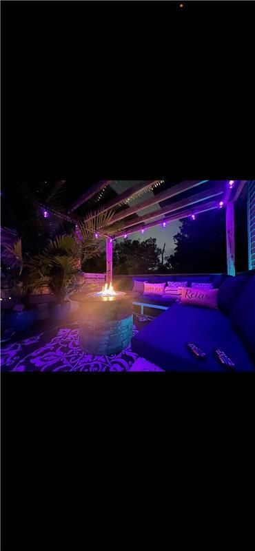 Outdoor patio with purple lighting, fire pit, and seating at night.