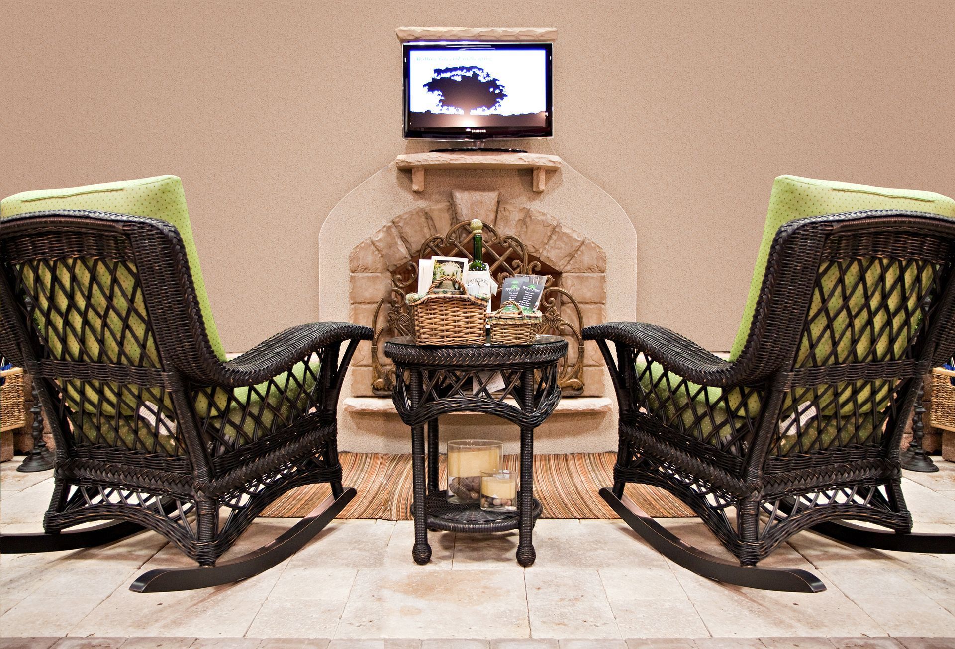 Two wicker rocking chairs with lime green cushions face a small round table in front of a stone fireplace with a TV.