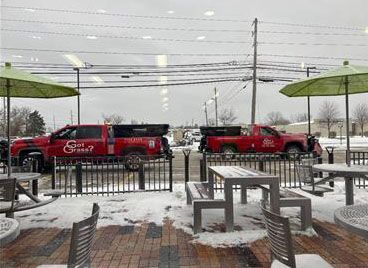 Two red pickup trucks parked outside a snowy outdoor patio area with green umbrellas and tables.