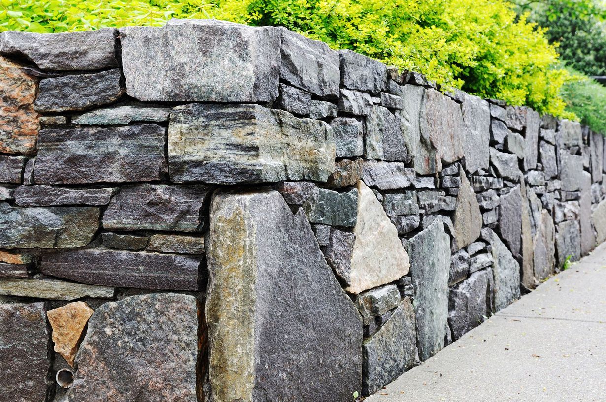 Stone wall with various gray stones; green foliage above.