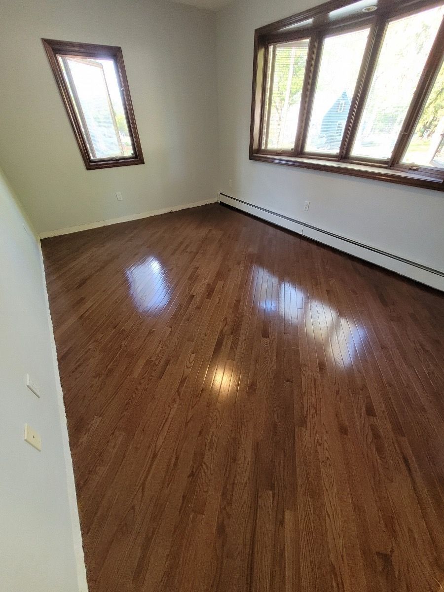 An empty room with hardwood floors and two windows.