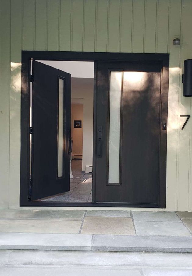 A black double door with vertical frosted glass panels is slightly ajar, showing an entryway to a home with a light floor.