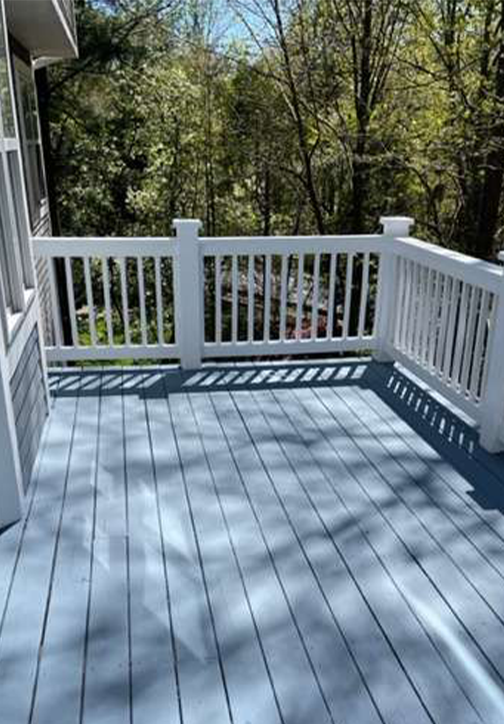 A light blue painted wooden deck with white railing overlooking a forest of green trees on a sunny day.