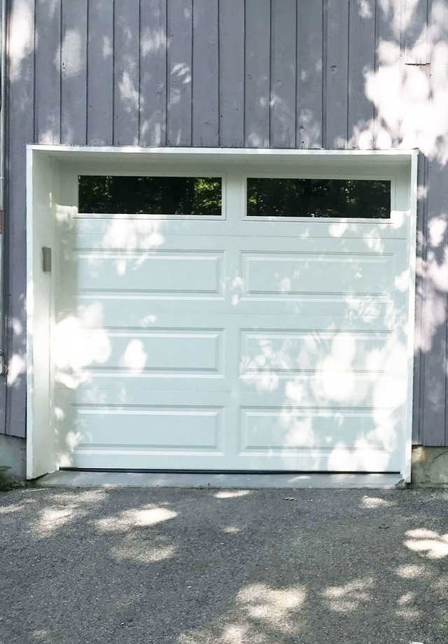 White single-car garage door with two top-row windows set in a gray paneled exterior wall.
