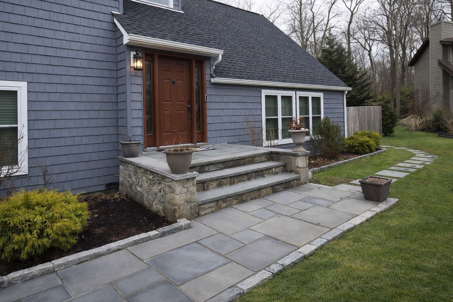 A blue-gray house with a brown door, stone steps, and a matching stone walkway leading through a green lawn.