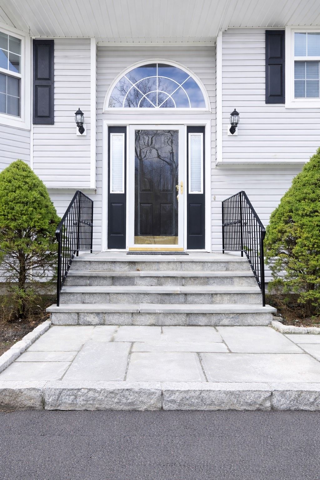 A home entryway featuring stone steps leading to a dark front door with a semi-circular transom window and black railings.