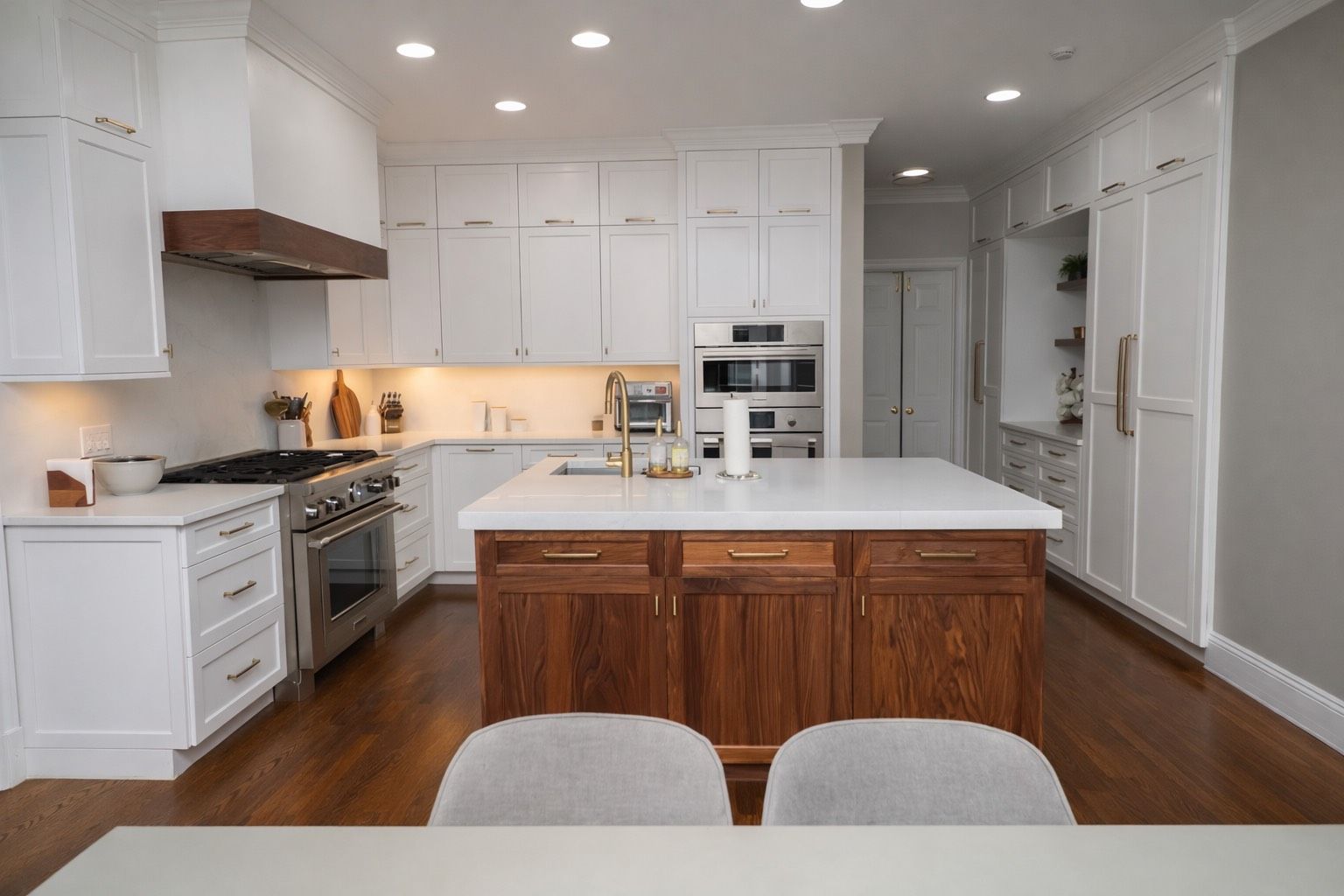 A modern kitchen with white cabinets, a wood-toned island, stainless steel appliances, and dark hardwood floors.