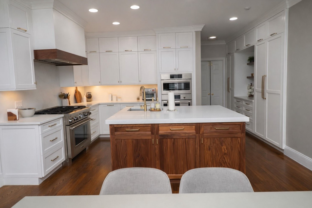 Modern kitchen with white cabinetry, a wood-toned center island with a white countertop, and warm wood flooring.