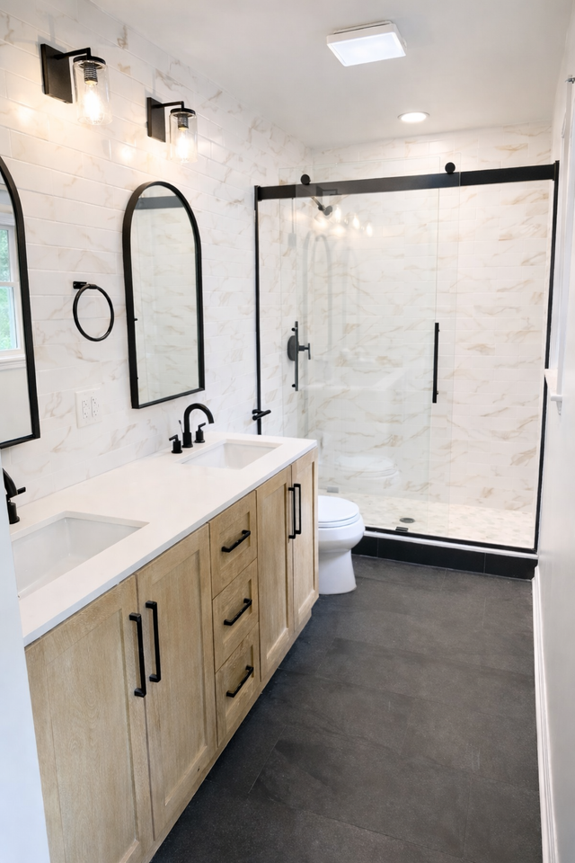Modern bathroom with light wood vanity, white marble walls, black fixtures, and a walk-in glass shower.