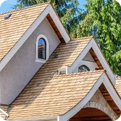 Close-up of a house exterior with light brown cedar shake roofing, light gray stucco walls, and arched window detailing.