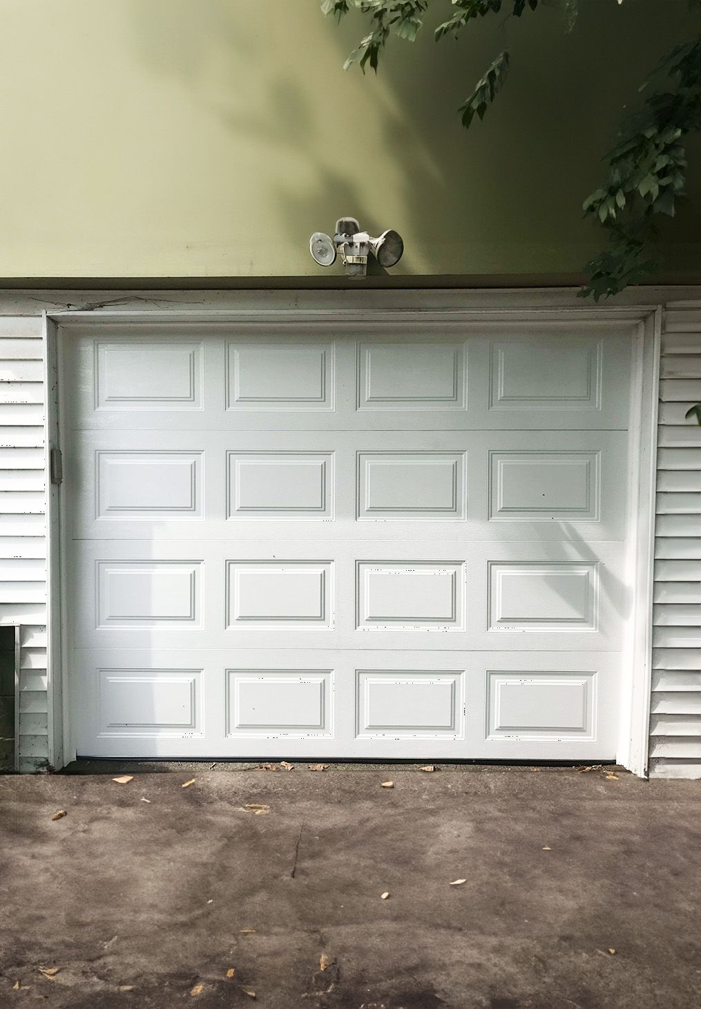 White garage door with four rows of rectangular panels on a suburban house exterior with siding and an outdoor light.