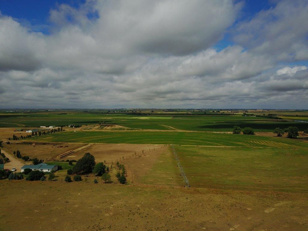 An aerial view of a lush green field with a house in the distance.
