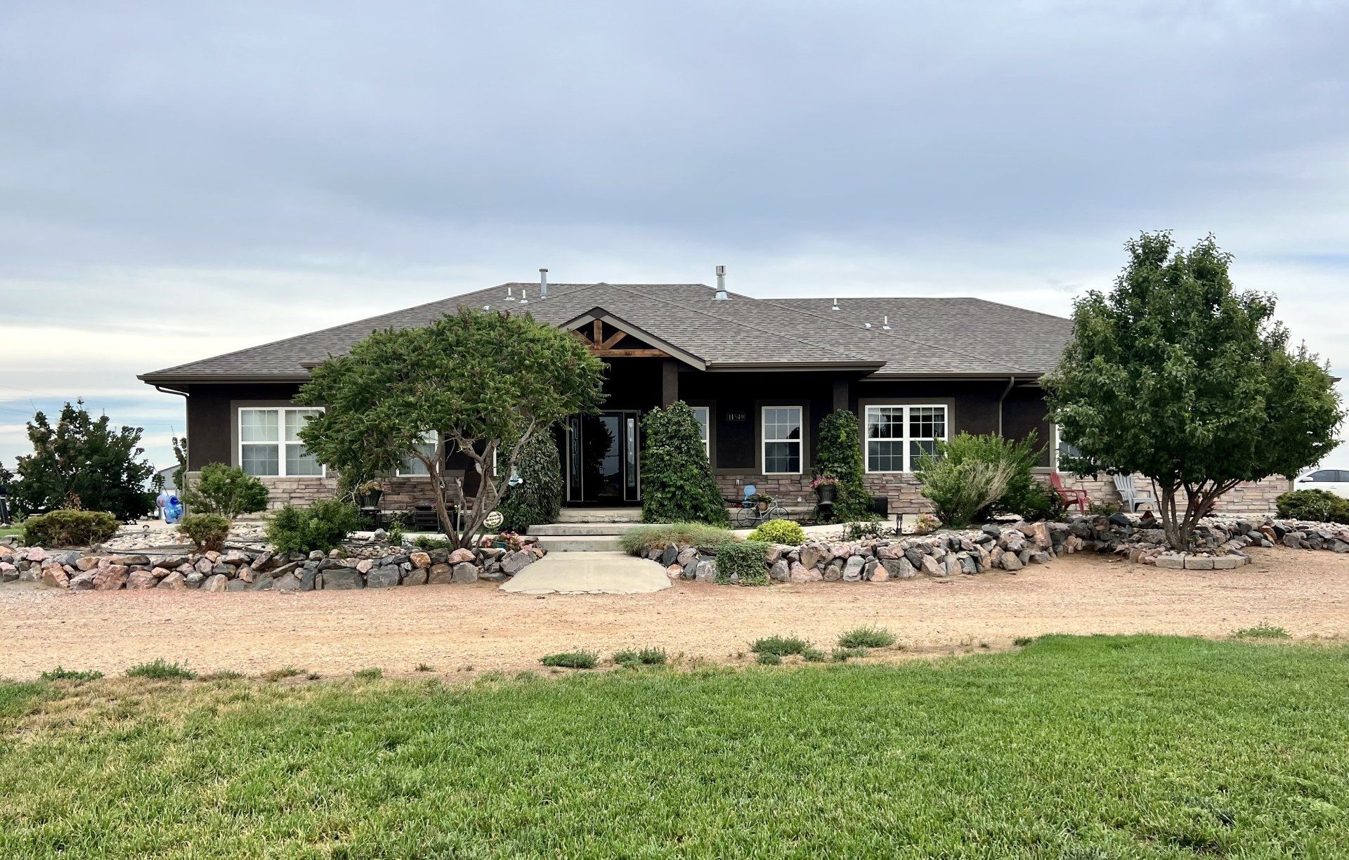 A large house with a gray roof is sitting in the middle of a grassy field.