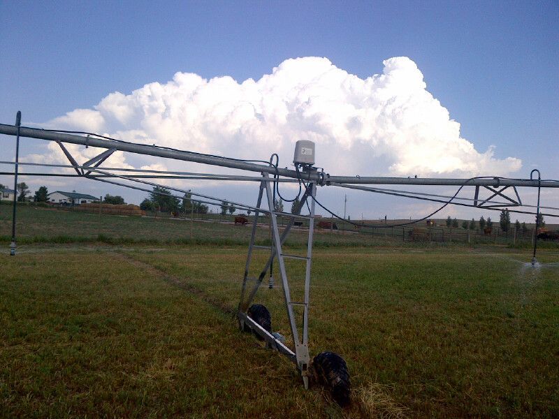 A sprinkler in a field with a cloudy sky in the background